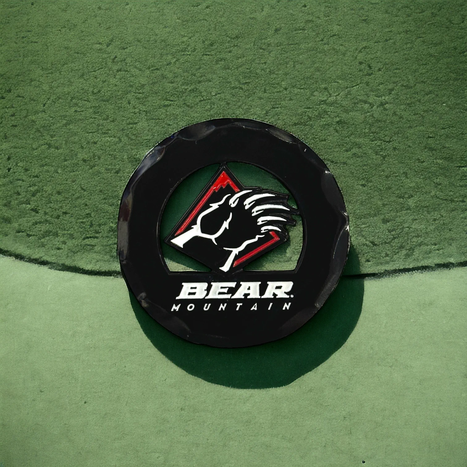 Black circular golf ball marker with the Bear Mountain bear claw logo in red and white.